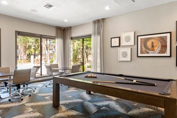 A pool table is in the middle of a room with a view of trees outside the window.